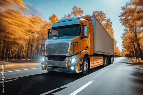 A truck drives through a forest in autumn. The trees are tall and yellow, and the sun shines brightly. The truck carries goods to its destination. © Ongushi