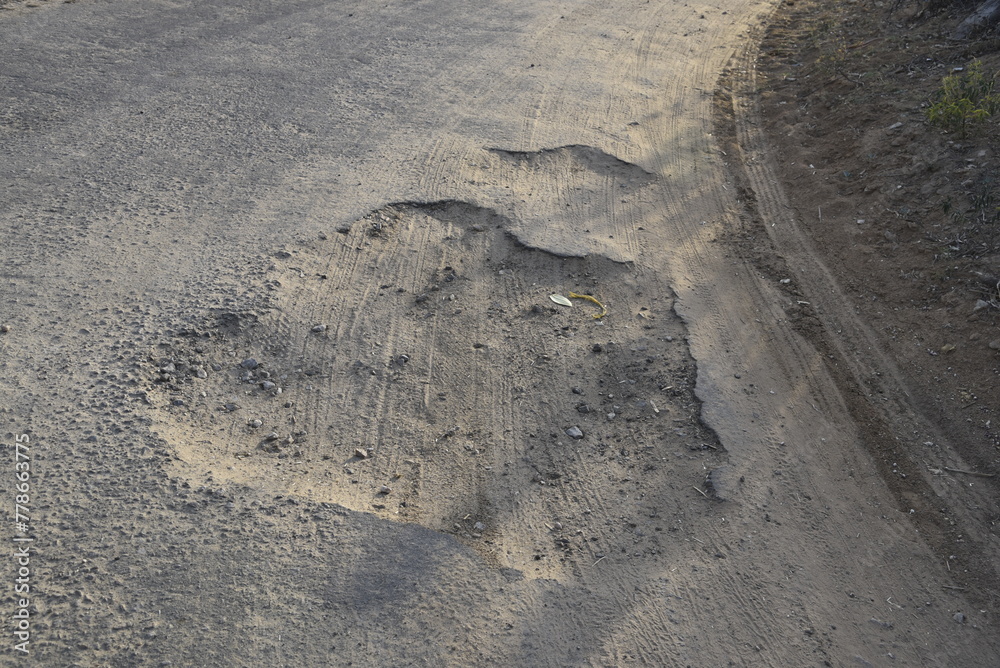 Bad road, cracked asphalt with potholes and big holes. Potholes on the road with stones on the asphalt. The asphalt surface is destroyed on the road. Bad condition of the road Bad road, cracked asphalt with potholes and big holes. Potholes on the road with stones on the asphalt. The asphalt surface is destroyed on the road. Bad condition of the road