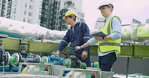 Two engineers with hard hats are checking the gauge on a pipeline valve in an urban industrial