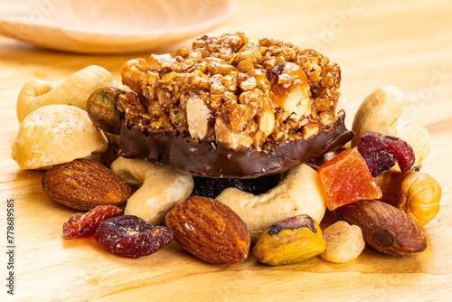 Closeup view of peanuts, almond and chocolate mini protein bars on pile of mixed fruits and nuts with wooden spoon on wooden board.