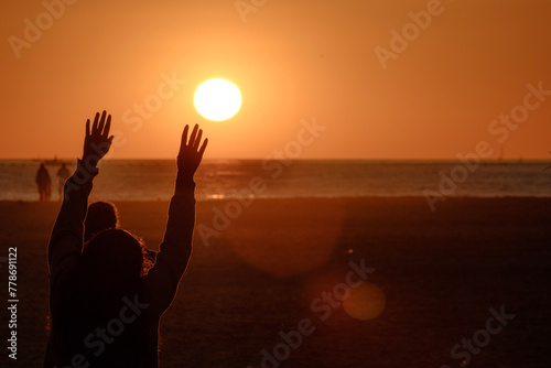 Playa de Tarifa, Cádiz, atardecer en la playa, personas disfrutando de los últimos rayos de sol en la arena de la palya, luz dorada, persona con las manos en alto, rozando el sol, alegría y fiesta
