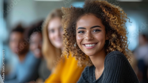 a close up of a person smiling with a group of people in the background in the background, there is a woman with curly hair in the foreground.