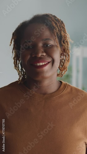 Positive African American woman shows friendly attitude standing against bright lamp at home. Portrait of lady looking in camera with white-toothed smile closeup photo