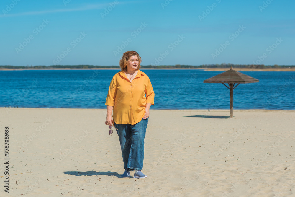 Vacation mood. Plus size happy mature lady wear yellow shirt and blue pants at beach , spring - summer clothes collection