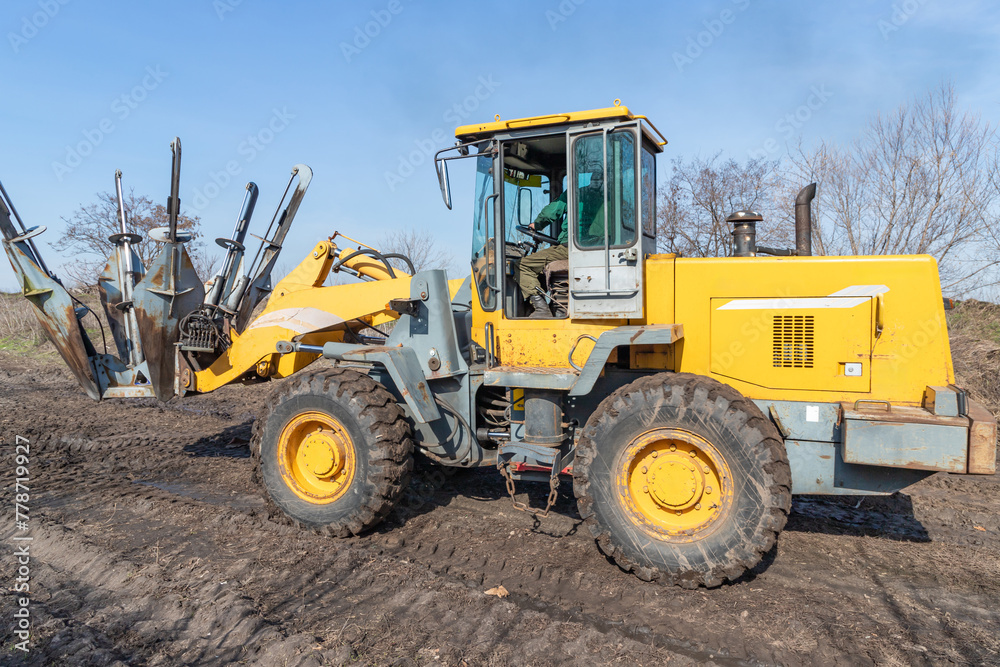 Male worker drives tree transplanter heavy machine. Landscaping, seasonal agricultural engineering, large trees landing machines. Specialized machine for transplanting and transport trees.