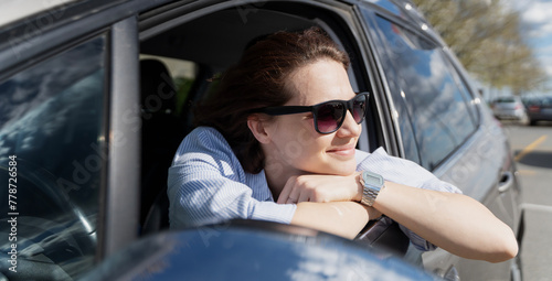 Smiling dreamy Caucasian woman in sunglasses sitting in a car on a summer day
