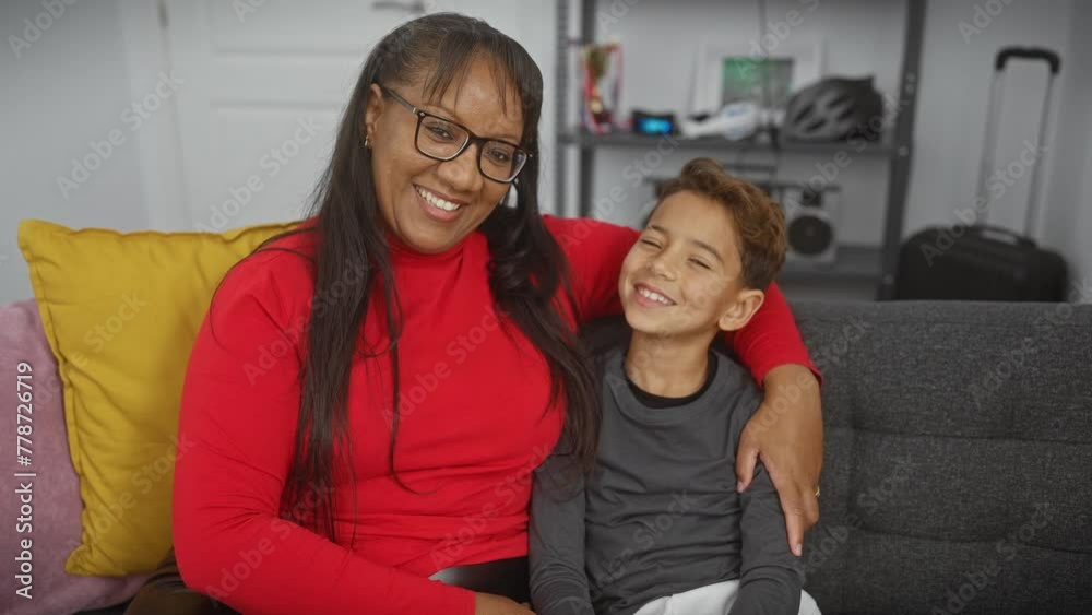 A smiling woman in red embraces a joyful boy on a couch, symbolizing motherly love in a cozy home setting. A smiling woman in red embraces a joyful boy on a couch, symbolizing motherly love in a cozy home setting.