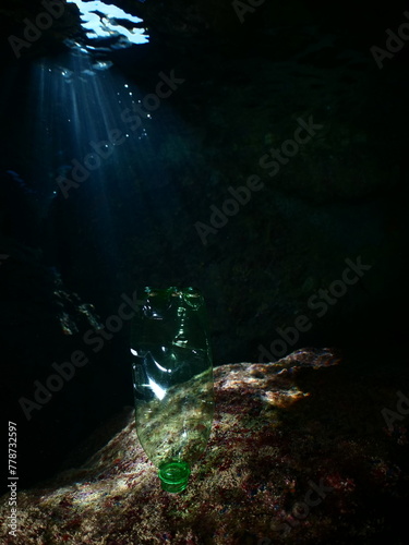 a green plastic bottle in a cave underwater ocean pollution with sun beams and rays