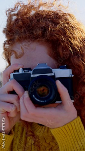 Portrait of young redhead woman taking a photo with a vintage camera. Teenager looking at camera.