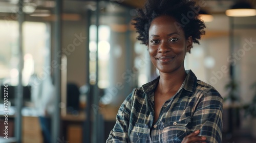 Easygoing woman with an updo hairstyle and a plaid shirt poses informally in an office space photo