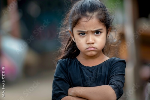 A young girl stands arms crossed, frowning, expressing dissatisfaction and stubbornness photo