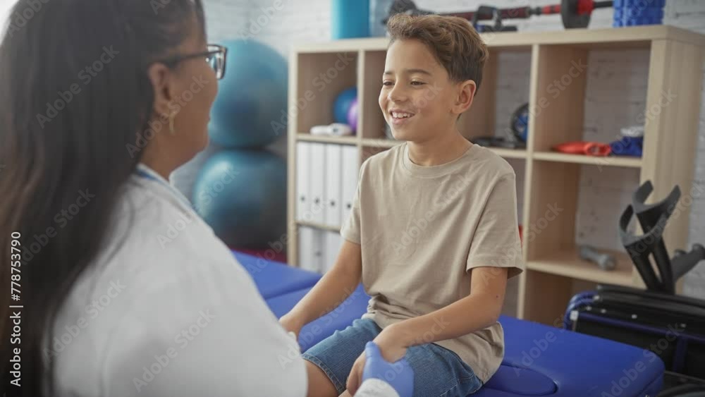 A smiling boy embracing a woman in a white coat indoors, depicting a warm moment between a child patient and a healthcare professional in a therapy room. A smiling boy embracing a woman in a white coat indoors, depicting a warm moment between a child patient and a healthcare professional in a therapy room.