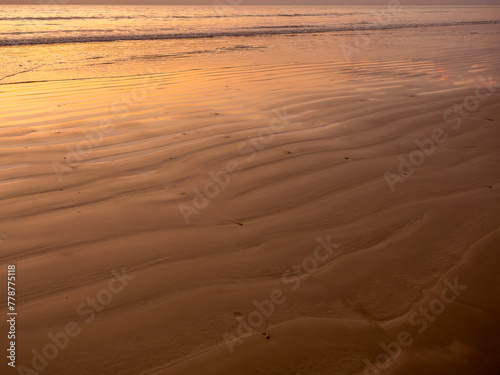 Sandy pattern and curved texture on the beach created by waves and sea breezes on sunset. Wet sand beach with peace sea water background for summer holiday and tropical travel vacation concepts.