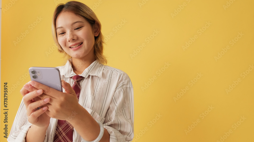 Smiling young woman wearing shirt and tie using mobile phone isolated on yellow background in studio Smiling young woman wearing shirt and tie using mobile phone isolated on yellow background in studio