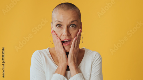 Close-up, shocked young hairless woman, looking at camera with big eyes, says wow, isolated on yellow background in studio photo