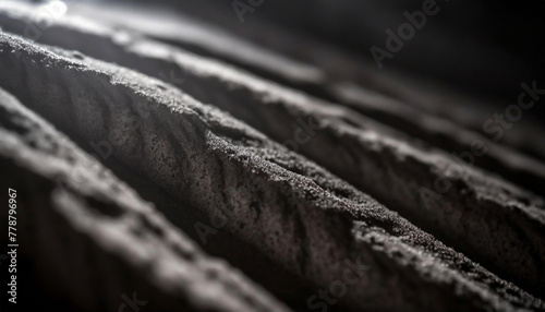 Close-up of abstract textured, dark stone surface with light highlighting the ridges, creating a dramatic and moody atmosphere. photo