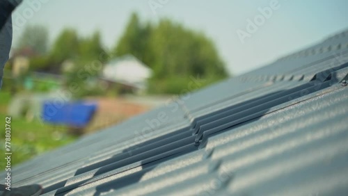 A roofer screwing a self-tapping screw into a black metal roof. Close-up of screwing a self-tapping screw into a metal roof.