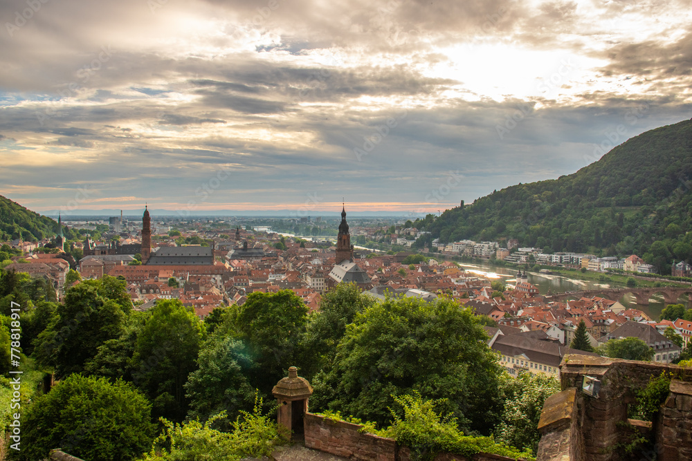 View over an old town with a castle or palace rune in the evening at sunset. This place is located in a river valley of the Neckar, surrounded by hills. Heidelberg, Baden-Württemberg, Germany