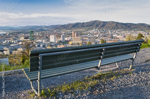 Park bench with a view of the city of Zurich in spring with the snowy Swiss Alps in the background from the Waid