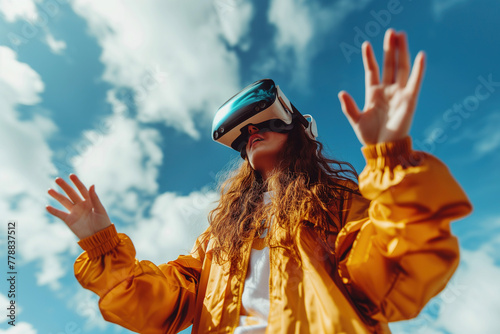 Curly-haired woman in VR glasses, gesturing towards the sky, lost in an virtual reality experience outdoors. Spatial augmented reality technology concept.