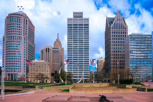 Detroit City vibrant skyline, high-rising buildings, modern plaza park with American Flags waving under dramatic white clouds in the blue sky in Michigan, USA photo