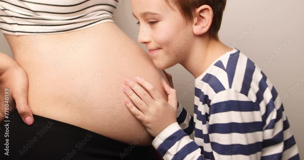 Little boy looking at her mother pregnant tummy. Pregnant mother and son spending time together at home. Pregnancy, family, parenthood, preparation and expectation concepts.