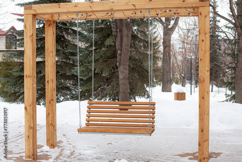 Wooden, large, hanging swing on a chain in the park. An empty swing in a winter park. The concept of loneliness.