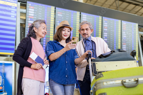 Group of Asian family tourist passengers with senior parent looking at the departure table at airport terminal for airline travel and holiday vacation
