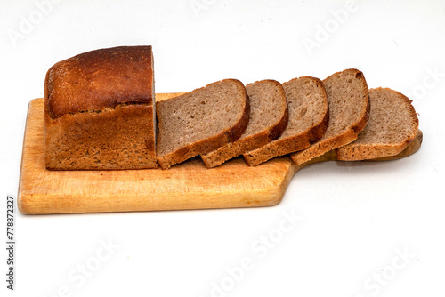 Slices of dark wholemeal bread next to a loaf on wooden chopping board © Tatty