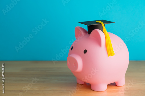 Pink piggy bank and mortarboard on wooden table with blue background copy space. Money savings and financial planning for education in university, college or international abroad study concept.
