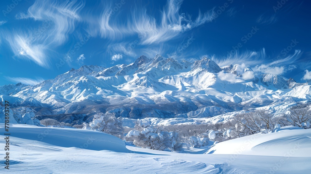   A mountain range covered in snow under a blue sky with wispy clouds