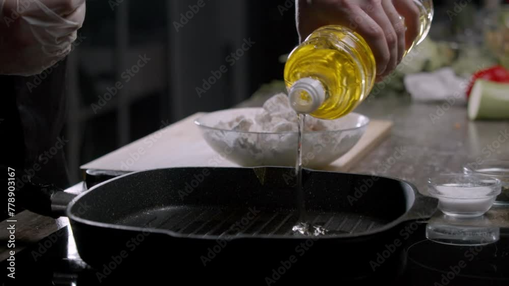 A chef in gloves pours vegetable oil into an extremely hot black frying pan. Then they add pieces of uncooked meat that have been dredged in flour and cook it. Close up. Slow motion. 4k A chef in gloves pours vegetable oil into an extremely hot black frying pan. Then they add pieces of uncooked meat that have been dredged in flour and cook it. Close up. Slow motion. 4k