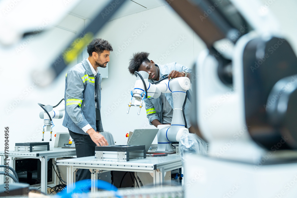 Naklejka premium Manufacturing, industry technology and science concept. Male technician engineer teamwork checking and maintenance electric robotic machine arm system with computer software in factory laboratory.