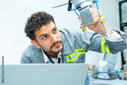 Manufacturing, industry technology and science concept. Professional male technician engineer checking and maintenance electric robotic machine arm system with computer software in factory laboratory.