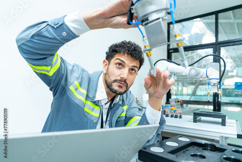 Manufacturing, industry technology and science concept. Professional male technician engineer checking and maintenance electric robotic machine arm system with computer software in factory laboratory.