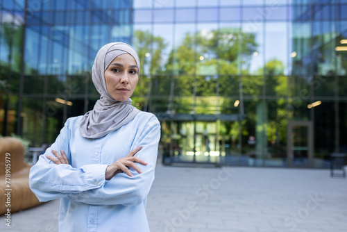 Professional Muslim woman with arms crossed in front of modern corporate architecture, exuding confidence and determination. © Liubomir