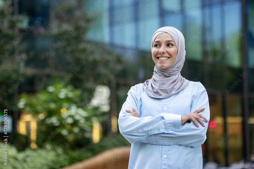 A professional young woman wearing a hijab confidently smiles against a modern office building backdrop, embodying inclusivity and diversity in the workplace.