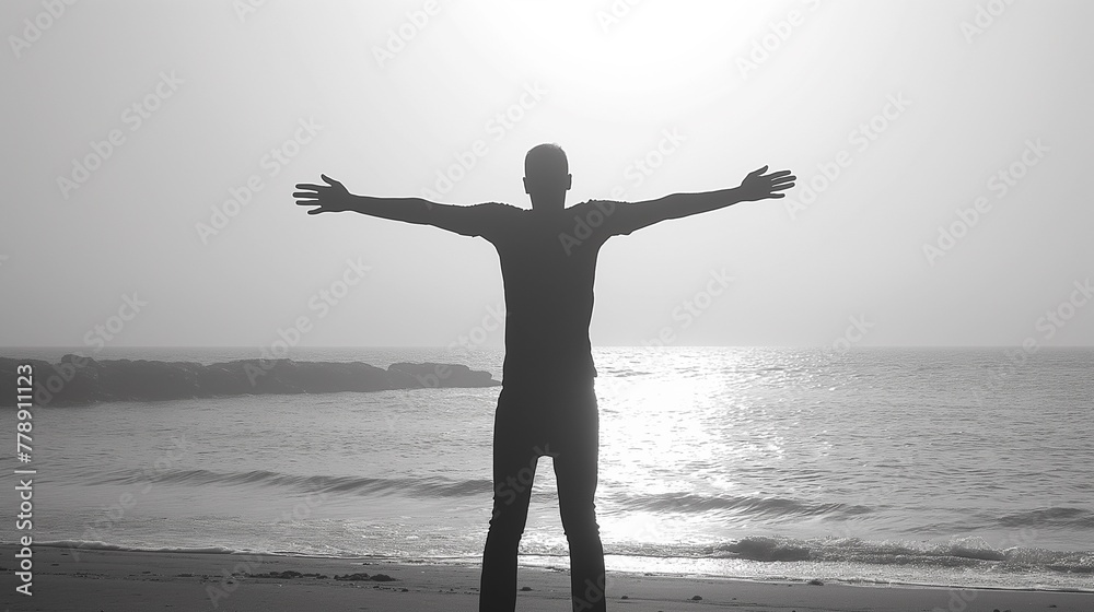 Obraz premium A man stands with his arms outstretched on the beach sunset, silhouette style, monotone black-white