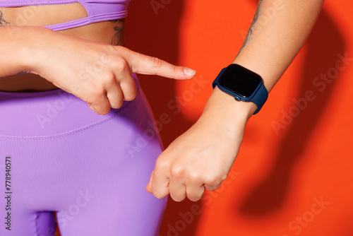 Close up cropped young fitness trainer sporty woman sportsman wear purple top clothes in home gym point on blank screen smartwatch isolated on plain orange background. Workout sport fit abs concept.