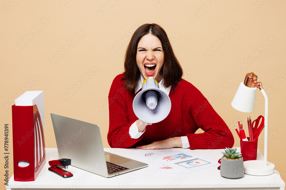 Young mad employee business woman wear red sweater sit work at office desk with pc laptop hold megaphone scream announces sale Hurry up isolated on plain beige background. Achievement career concept. - obrazy, fototapety, plakaty 