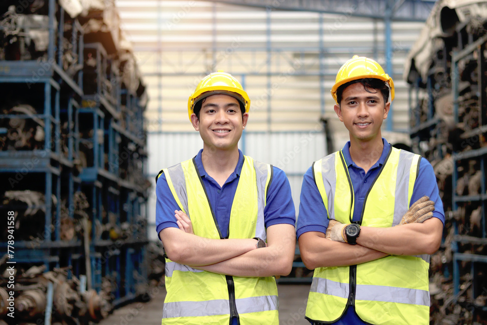 Portrait of two happy smiling Asian industrial engineer worker men with safety vest and helmet standing with arms crossed at manufacturing plant factory with many engine parts as blurred background. Portrait of two happy smiling Asian industrial engineer worker men with safety vest and helmet standing with arms crossed at manufacturing plant factory with many engine parts as blurred background.