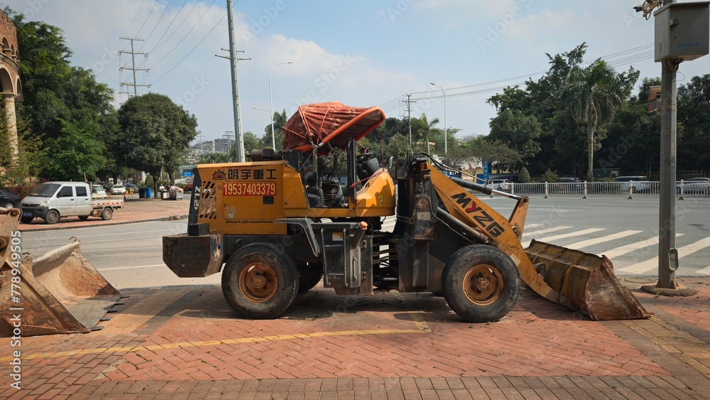 Front view of the open bucket of the machine - loader, delivering plants and tree seedlings from the nursery for landscaping city streets, city park. Seasonal transplant, landscaping service.