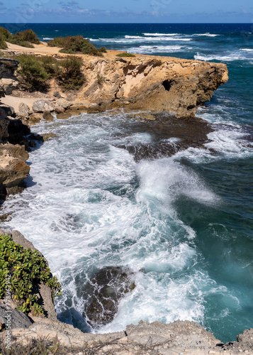 The turquoise waters of the Pacific Ocean slam against jagged rocks along the Mahaulepu Heritage Trail in Koloa, Hawaii on the island of Kauai.