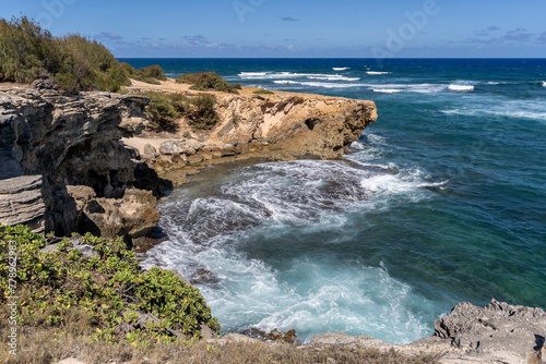 The turquoise waters of the Pacific Ocean slam against jagged rocks along the Mahaulepu Heritage Trail in Koloa, Hawaii on the island of Kauai. photo