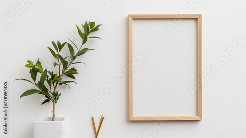 Minimalist composition with a wooden picture frame, green potted plant, and two pencils on a clean white background, leaving copy space. photo