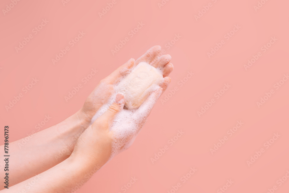 Naklejka premium Female soapy hands holding a piece of soap against a pink background.