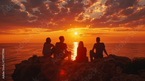 A group of people are sitting on a rock overlooking the ocean at sunset. The sky is filled with clouds and the sun is setting, creating a warm and peaceful atmosphere