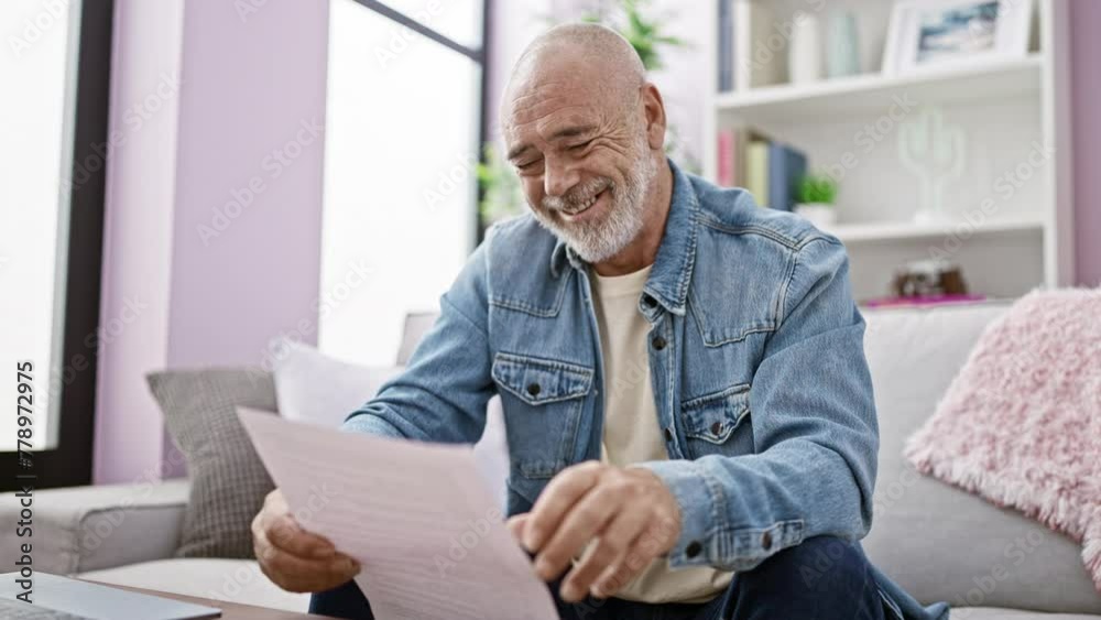 Smiling senior man with beard reading paper in a cozy, modern living room