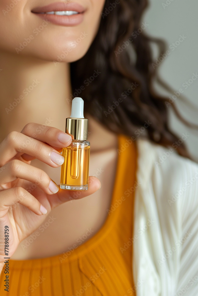 Fototapeta premium Young woman holding serum bottle with dropper. Beauty, cosmetics and skincare concept. Natural essential oil or favorite cosmetic product in glass bottle with pipette, everyday skin care routine