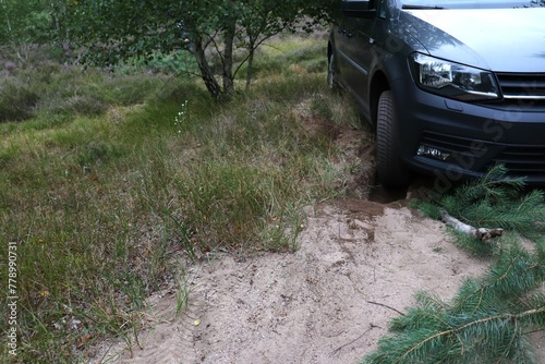 front tire of car lodged into ground surrounded by greenery, stuck vehicle. concepts: vehicle challenges, nature encounters, adventure gone wrong, unexpected challenges, stuck car tire, car trapped